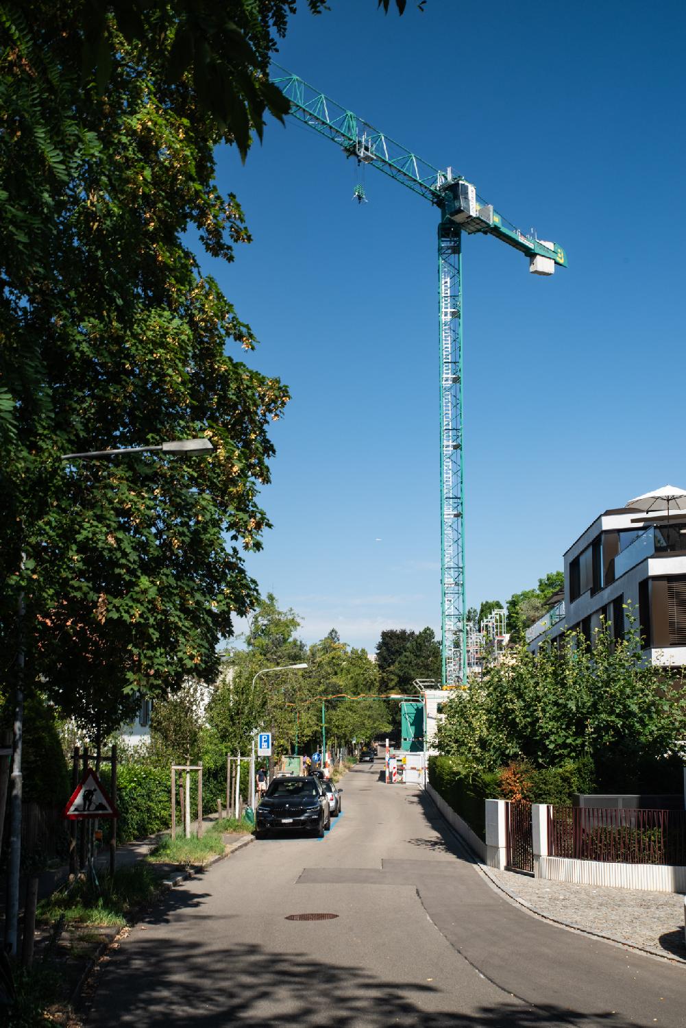 A narrow street with a large turquoise crane at the end of it