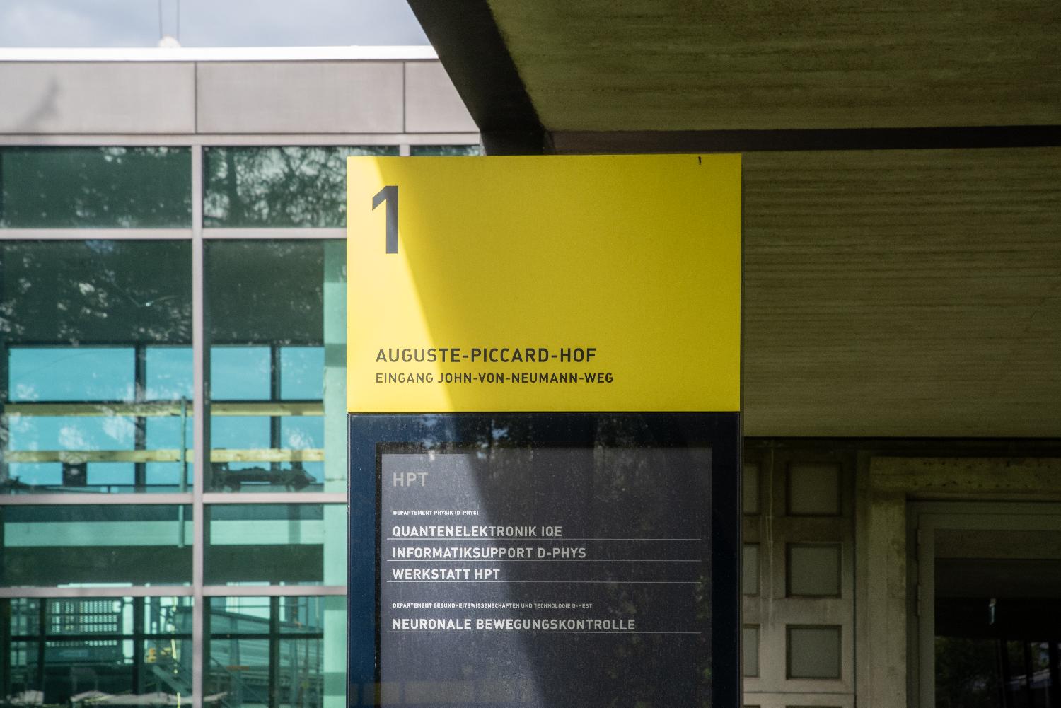 A sign at the entrance of a building, indicating 1 Auguste-Piccard-Hof, with mentions of various physics labs.