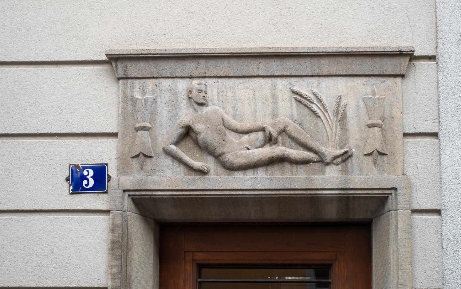 A relief on top of a wooden door, showing a man lying on the ground, with some wheat growing at his feet