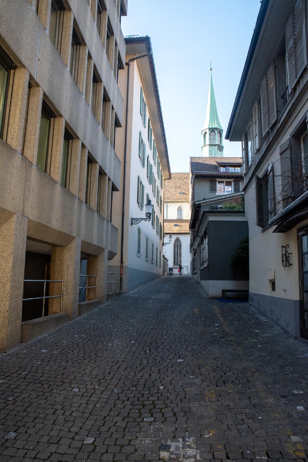 A paved alleyway with 3-4-story buildings on each side and a church building at the end of it