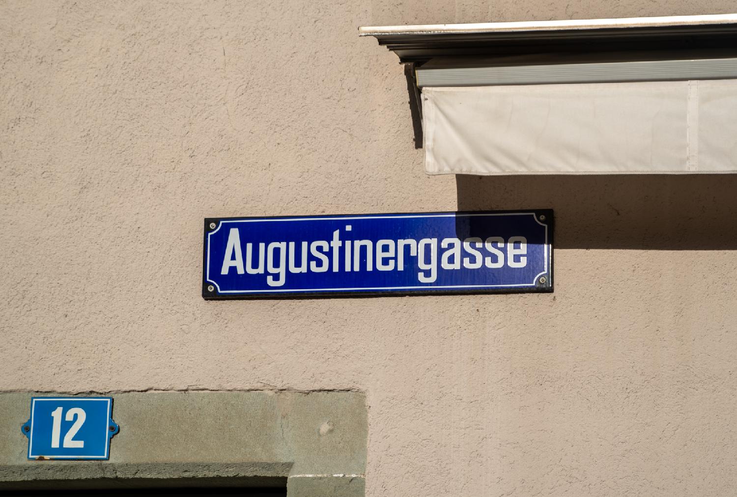 A blue "Augustinergasse" street sign on a concrete building wall