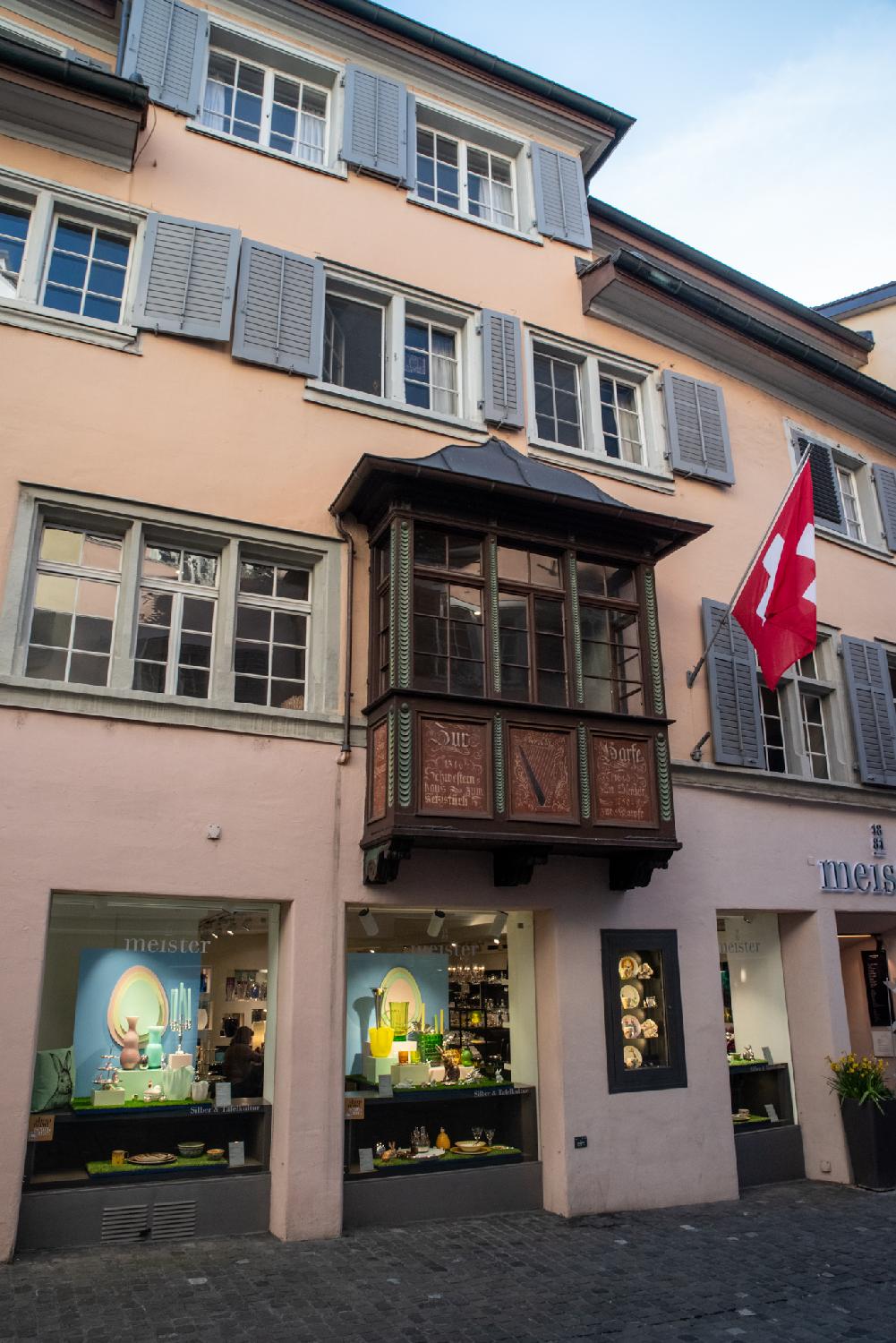 A rectangular oriel window protruding from a building with apartments and a shopfront.