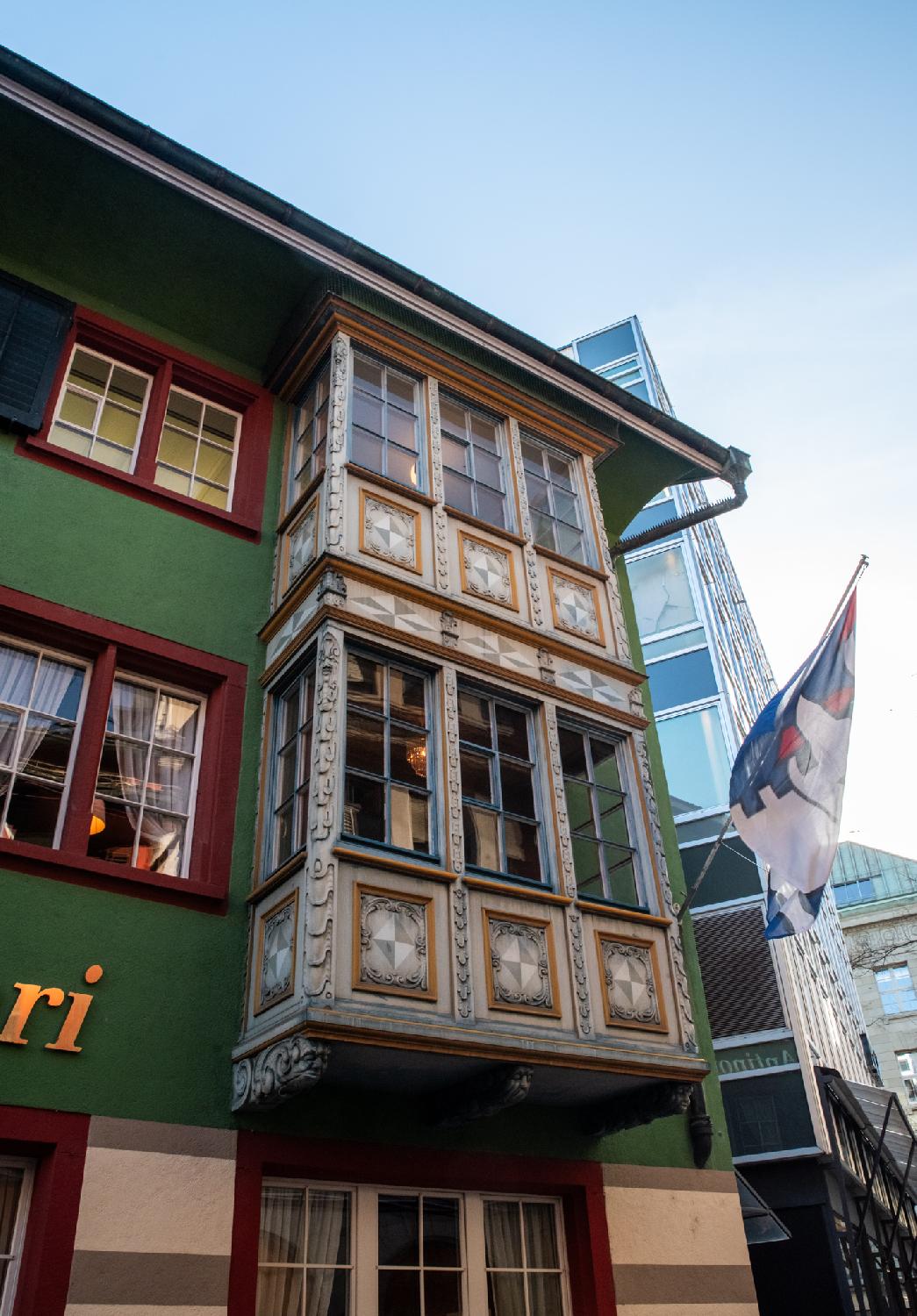 A two-storey ornate oriel window protruding from a dark green building