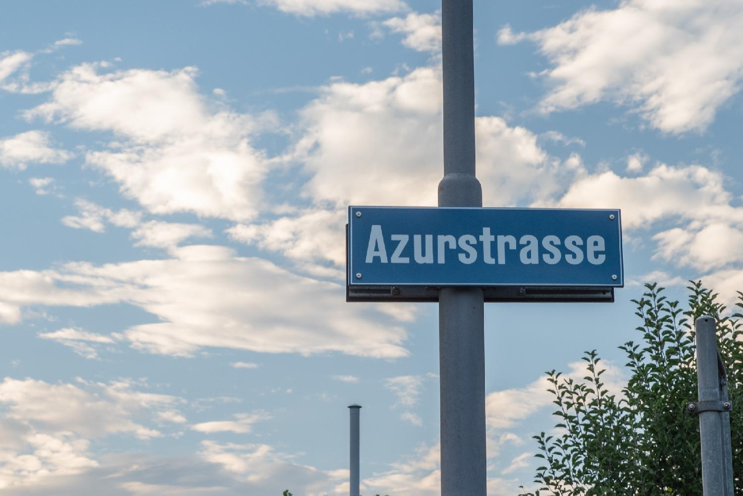 A blue "Azurstrasse" street sign on a metallic grey pole, with blue sky behind it