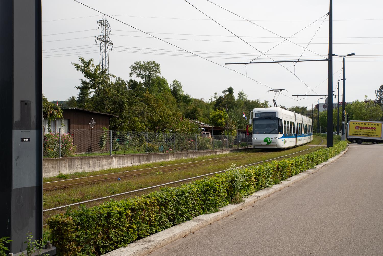 A Cobra tram line 10 on a railway passing through grass, next to a road