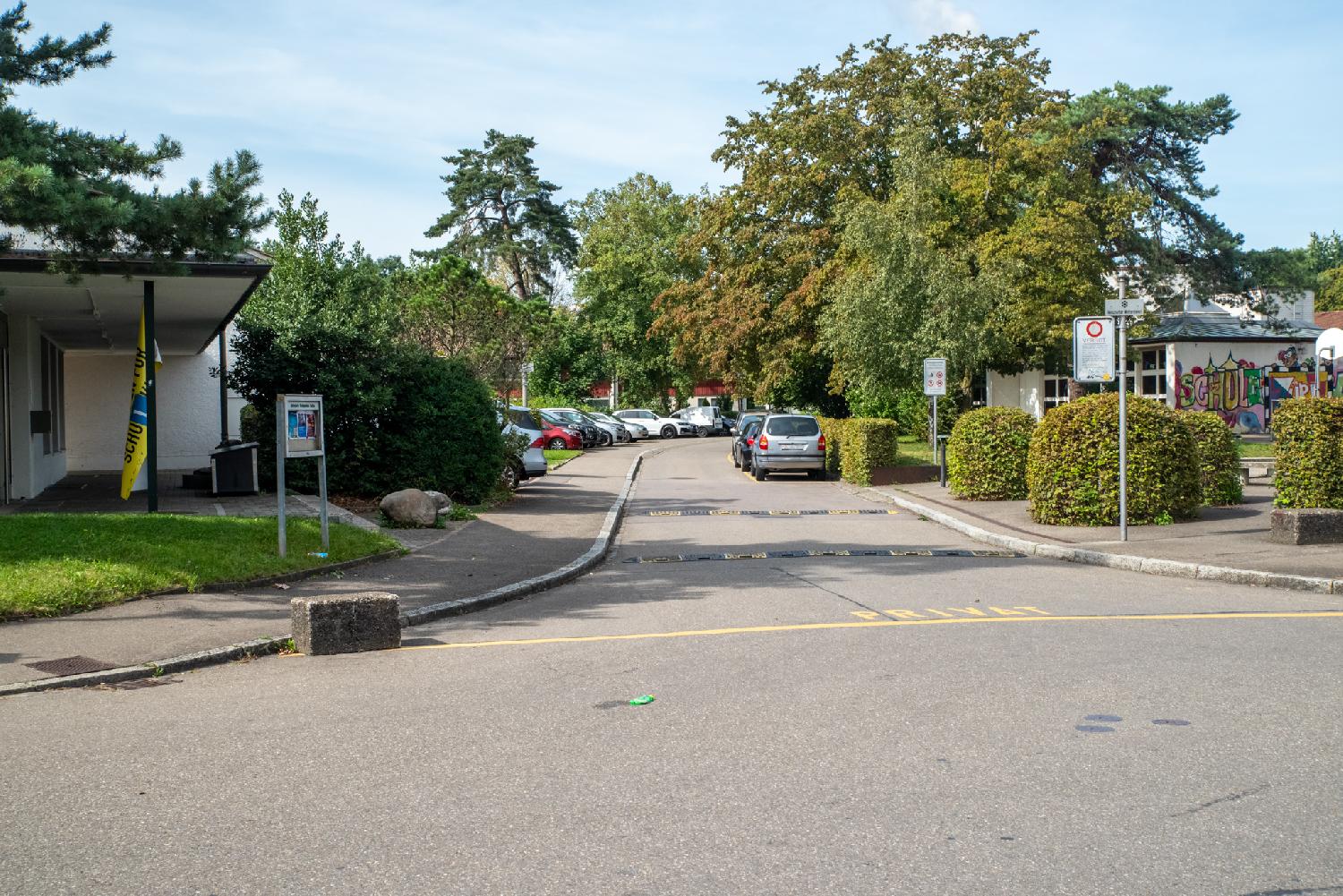 A small residential street with school and daycare, trees and parking lots in the background. The street has a yellow "Privat" line painted on the ground.