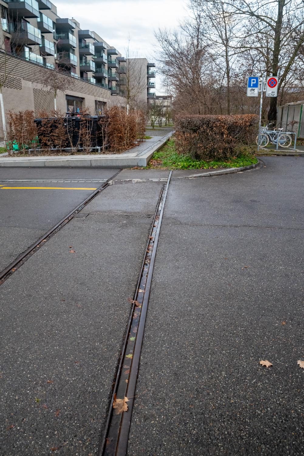 On the foreground, rail tracks that stop abruptly when intersecting a sidewalk. In the background, residential buildings with blue-tinted glass balconies.