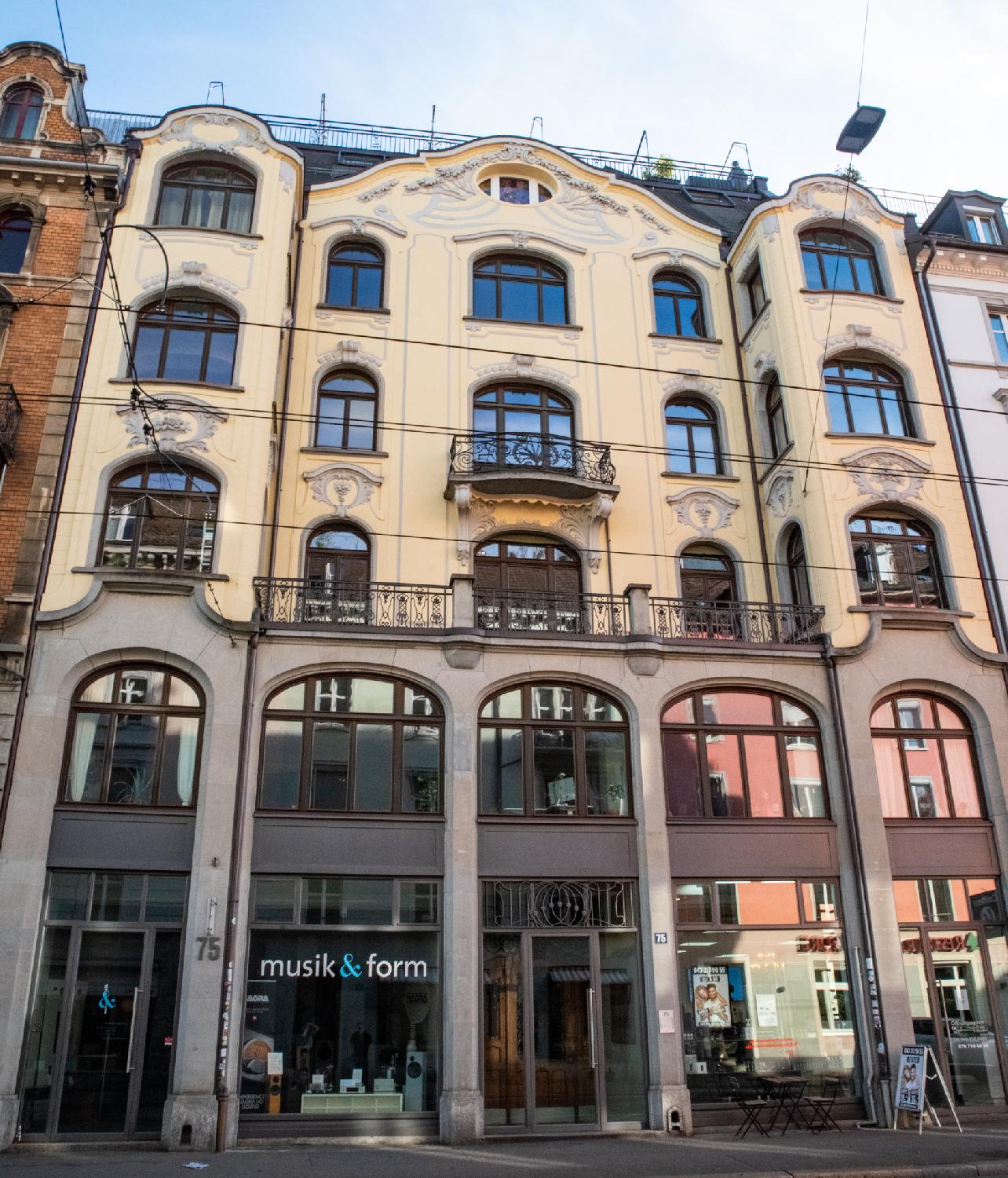 An Art Nouveau building with two stories made of large windows and three stories with curved windows on a light yellow wall.