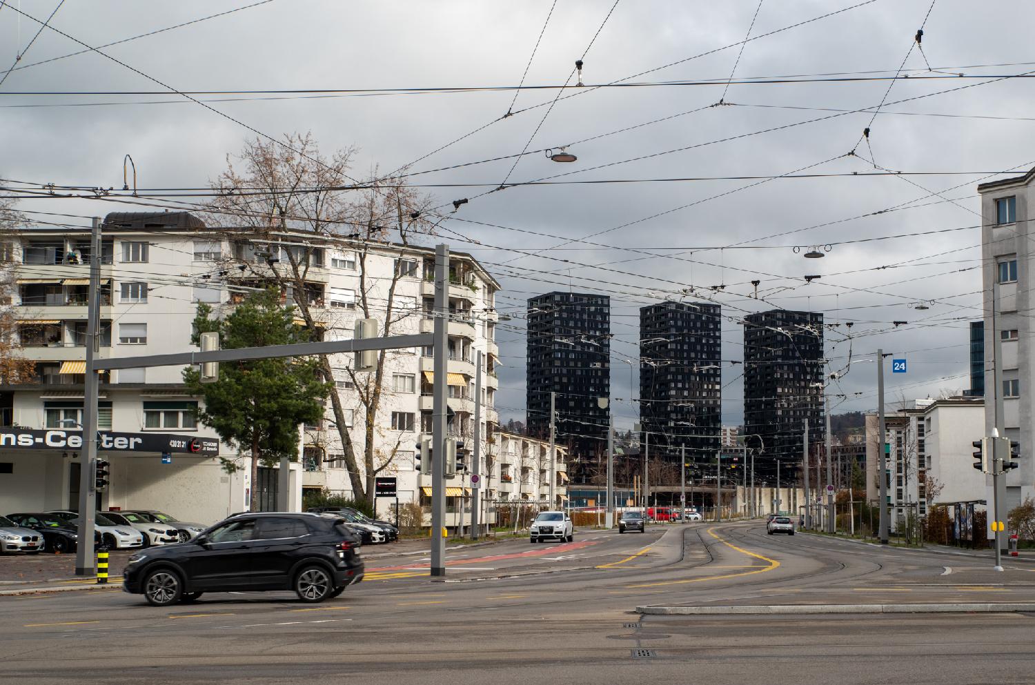 A street intersection with a large amount of tram cables and three black high-rise buildings in the background