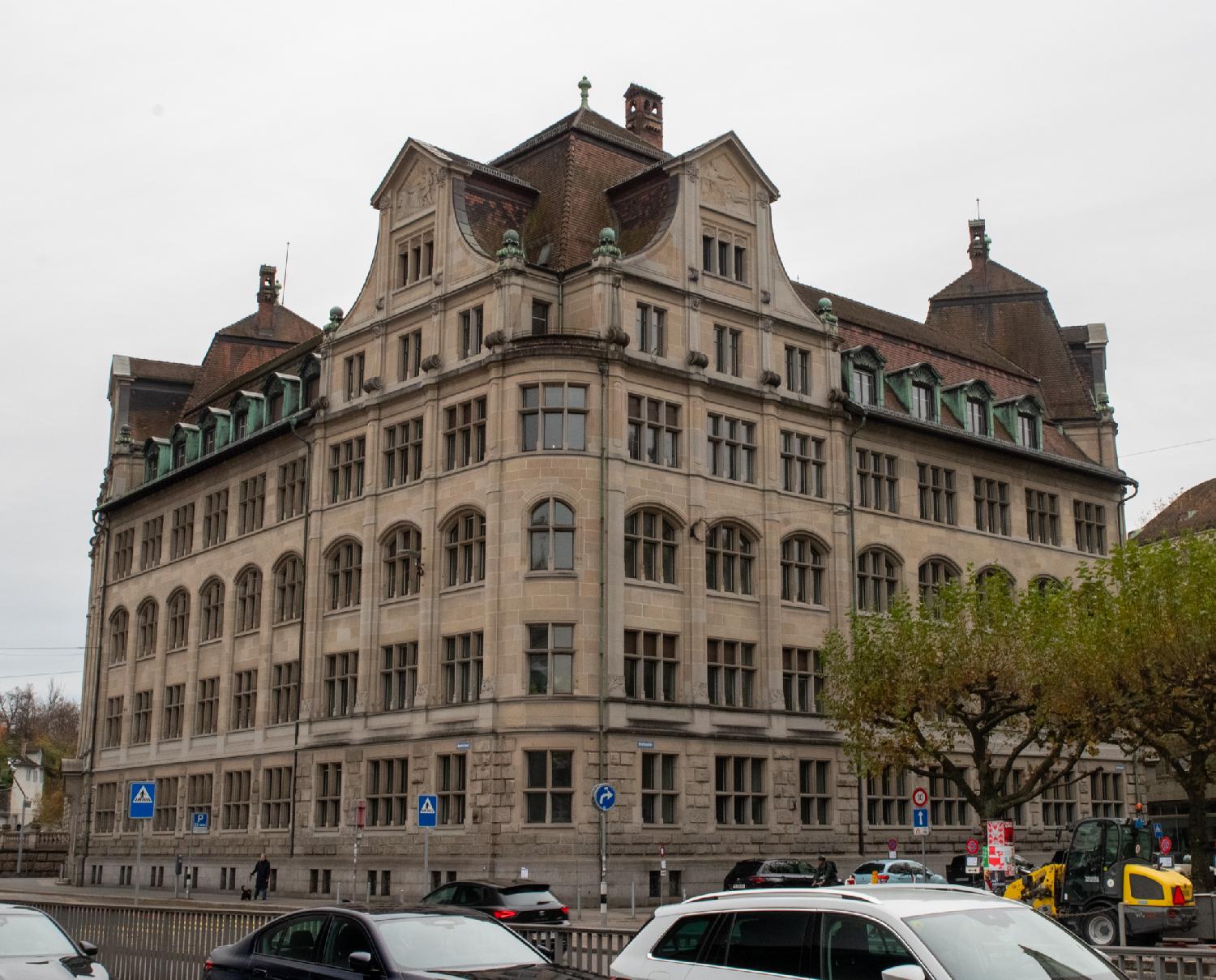 A large 6-story corner building, with a lot of windows, dormer windows on the roof and larger structures on rounded corners.