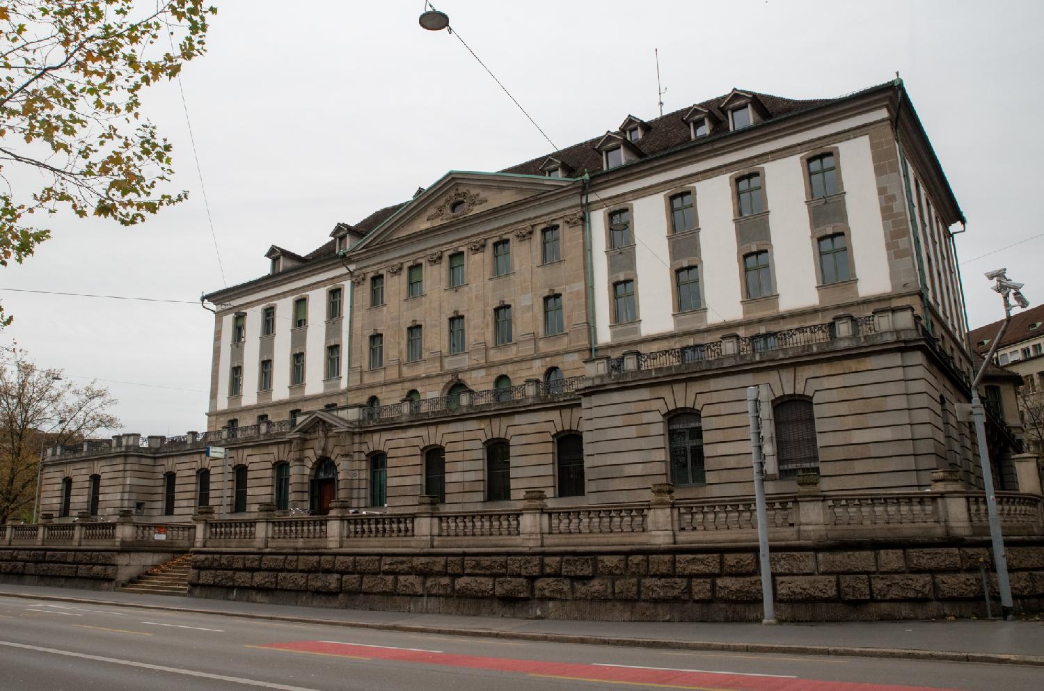 A large 5-6-story building, with two levels of dormer windows on the roof, a balcony/terase above the ground level and triangular pediment in the middle of the building.